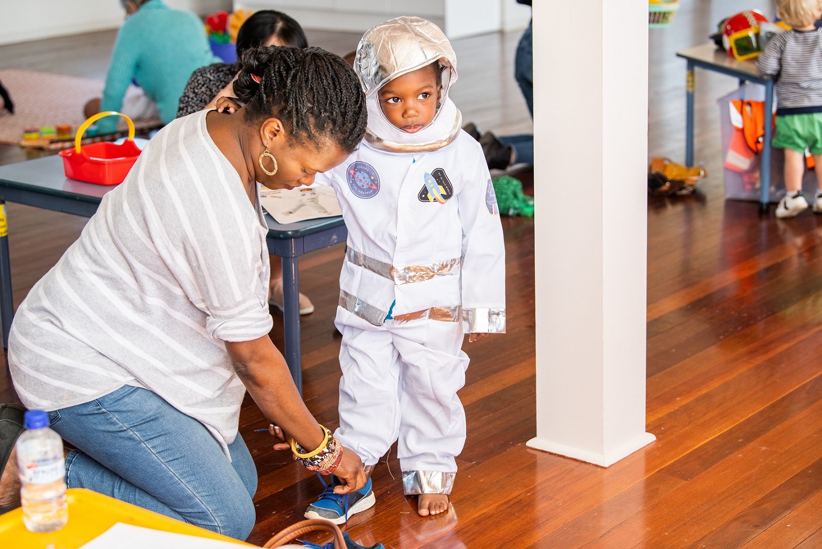 Parent tying shoes of child engaged in imaginative play dressed as an astronaut.