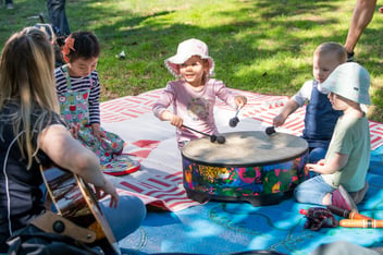 Children playing a drum together while a Play Matters Australia Music Therapist plays guitar
