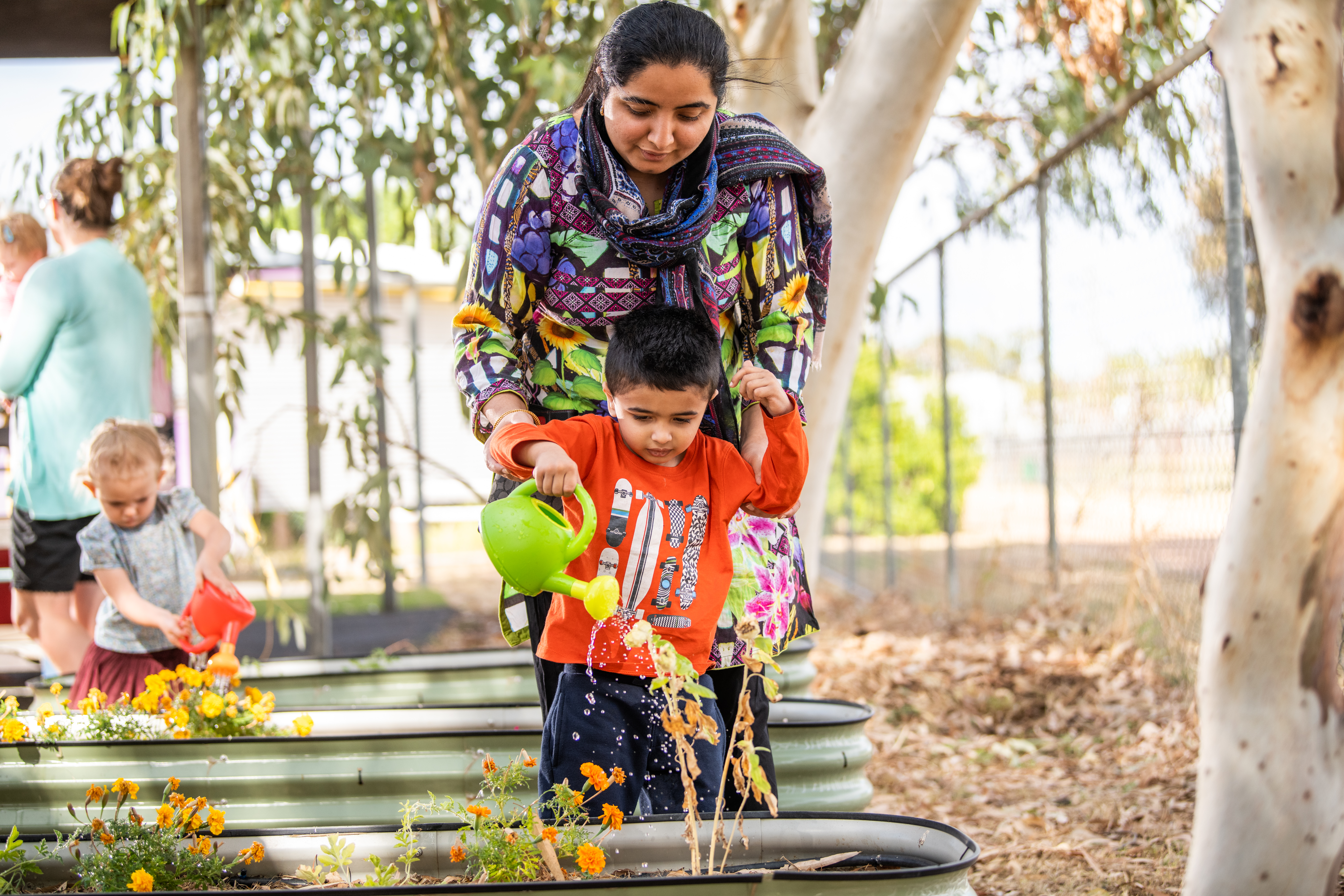 Child watering garden with parent