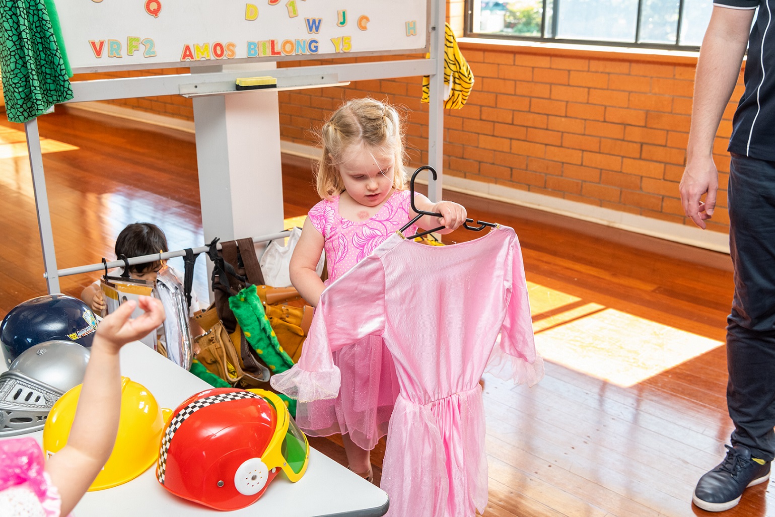 Child preparing for imaginative play by selecting a costume from playgroup dress up box.