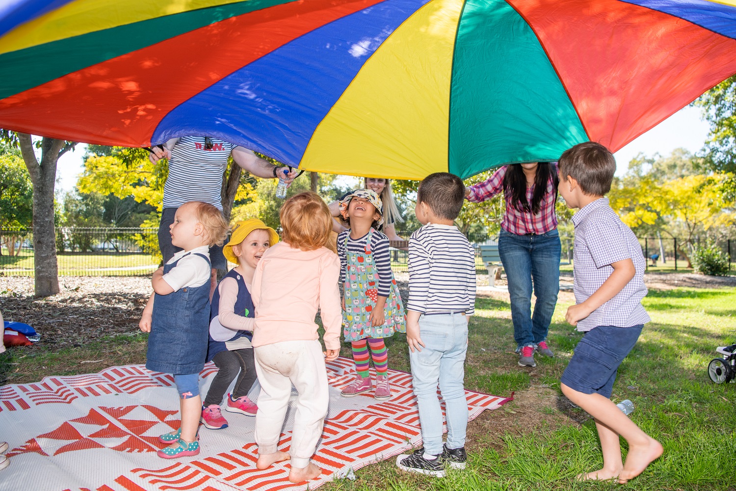 Children enjoying parachute play at playgroup in a local park